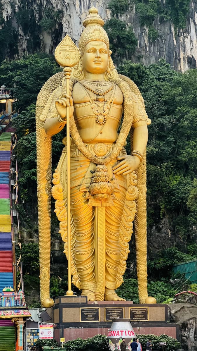 Golden Lord Murugan statue at Batu Caves with 272 rainbow stairs and limestone cliffs Malaysia Hindu temple